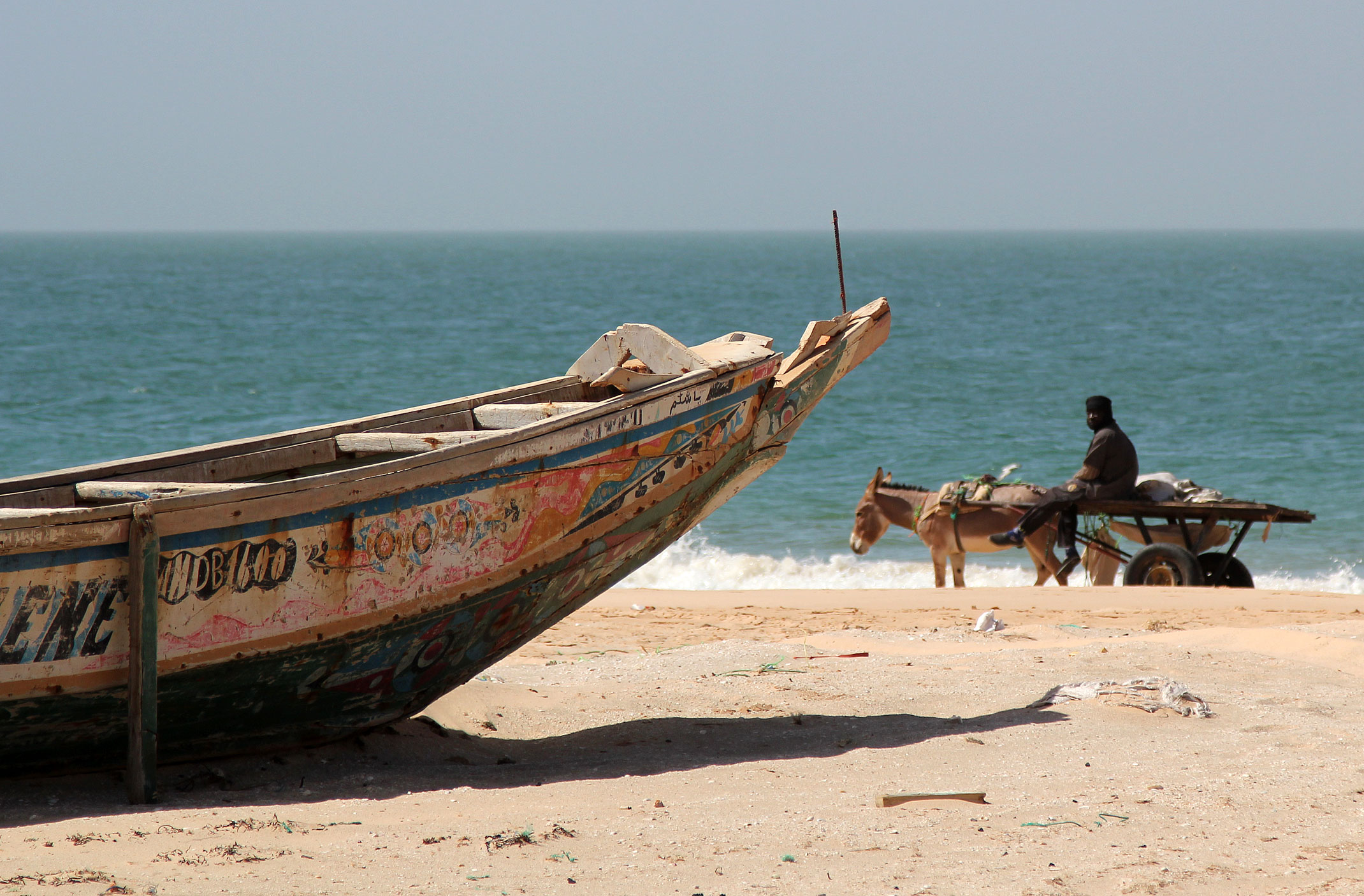 Mauretania.Kolorowa łódź nad brzegiem Oceanu Atlantyckiego i osioł ciągnący wózek.